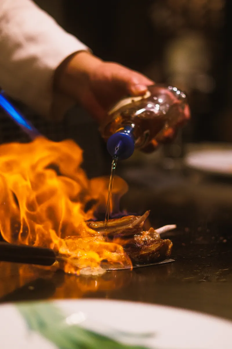 Flames rise around food cooking on a flat metal griddle