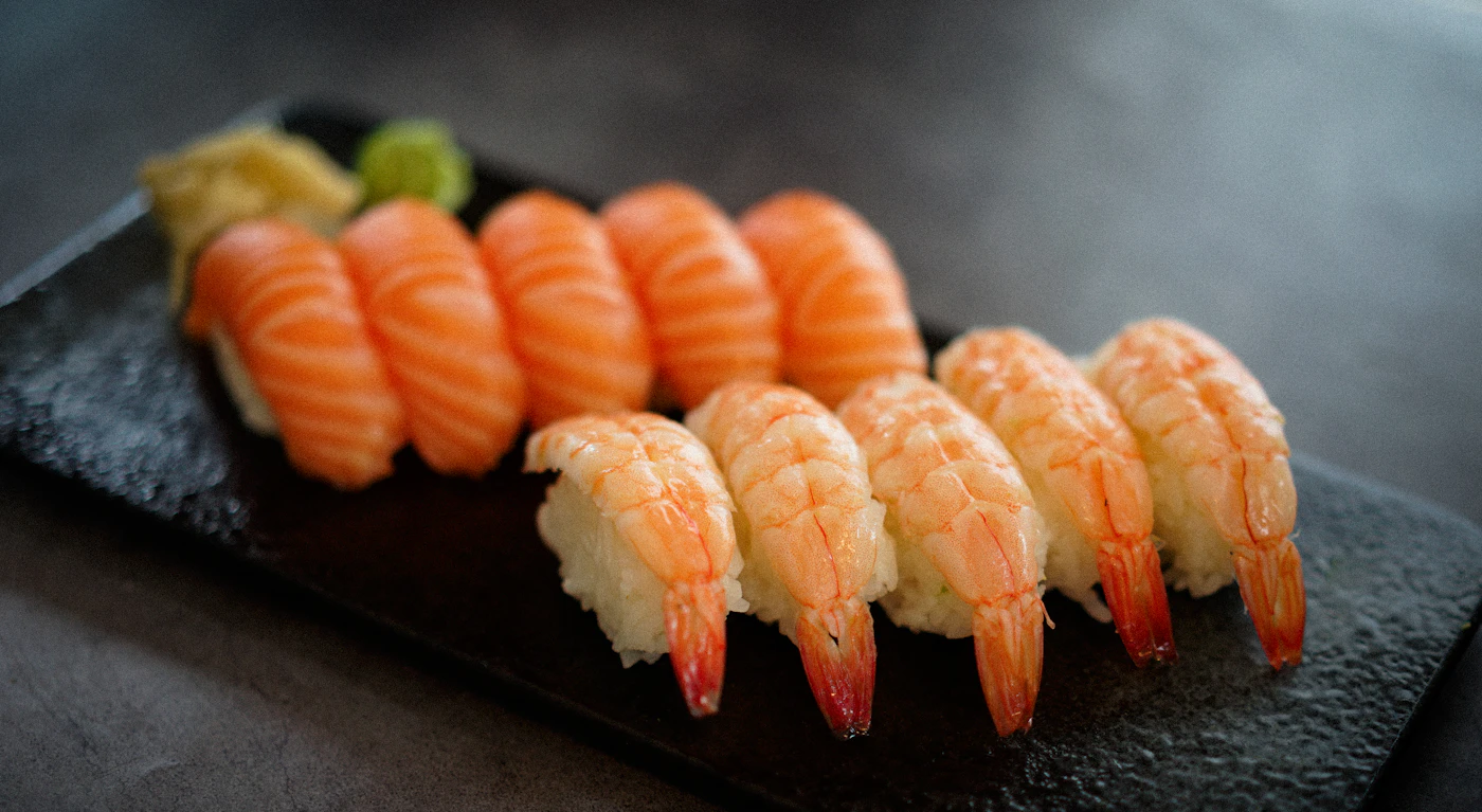 Shrimp and salmon nigiri arranged in two rows on a dark platter